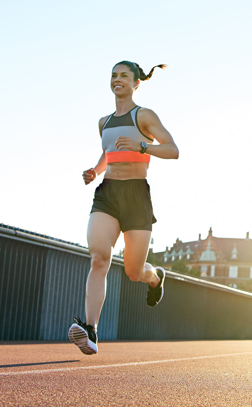 Smiling woman running outdoors in running shorts at sunset